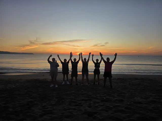 A Let Luce retreat group on a beach at dawn, arms raised against the sunrise.