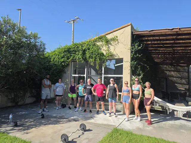 A Let Luce retreat group standing together on a sunny patio outside a villa, barbells on the ground in front of them.