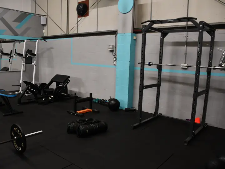 A black power rack with a barbell, a weight bench, a stack of weight plates and a barbell on the rubber floor.