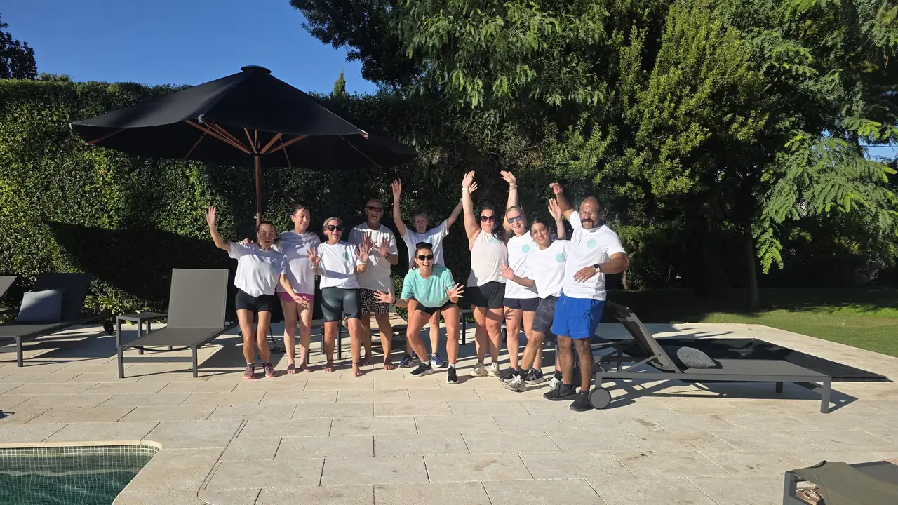 The retreat group cheering on the sun terrace by the pool, with parasols and a hedge behind.