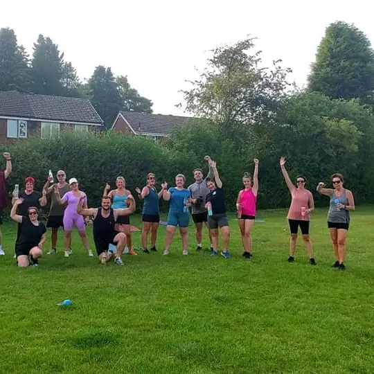 Lucy's crew on a grass field in daylight, many with their arms in the air.